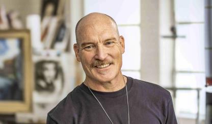 Photograph of Kevin Kibsey in studio setting holding a handful of paintbrushes is by Paul Markow.