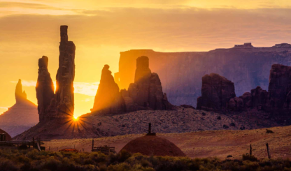 The sun peeks between the iconic spires of Monument Valley Navajo Tribal Park. By David Muench
