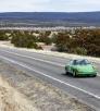 A green sports car cruises down a highway.