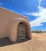 The adobe walls of S'edav Va'aki Museum are shown against a bright blue sky with whispy white clouds.