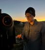 A young man in a black beanie and glasses calibrates a large telescope.
