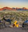Photograph of four people sitting around a fire at dusk with a view of the nearby Santa Rita Mountains is by Steven Meckler.