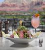 Photograph of an artistic salad and a pink drink garnished with flowers against a soft backdrop of a red rock view is by Rob Ballard.