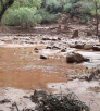 A color image shows the aftermath of flash flooding in the grand canyon and includes muddy water, debris and the remnants of a foot bridge.