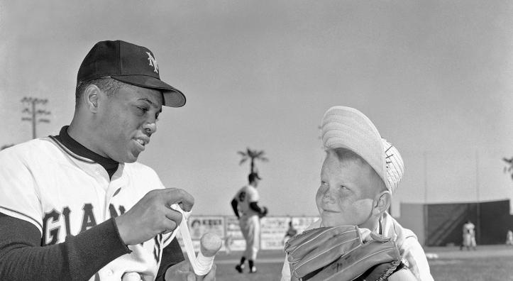 Baseball player wraps a bat as a child looks on.