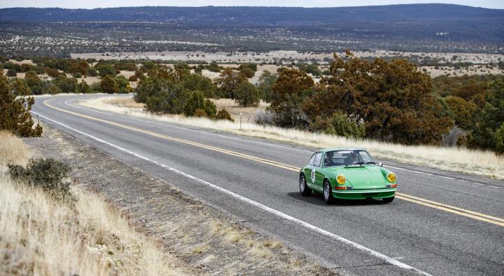 A green sports car cruises down a highway.
