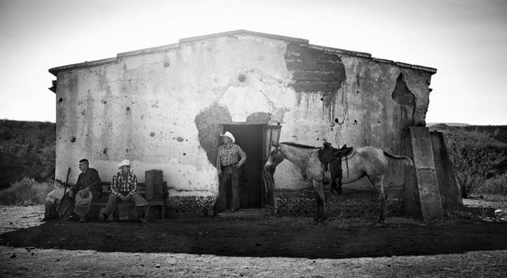 Cowboys stand in front of a ranch building in this black and white photograph