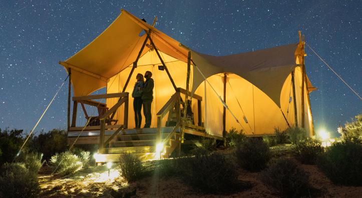 Campers look at a starry sky from beneath a canvas tent.