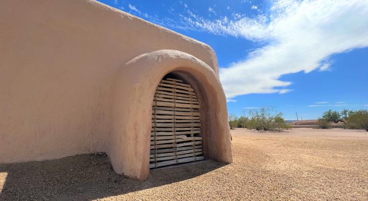The adobe walls of S'edav Va'aki Museum are shown against a bright blue sky with whispy white clouds.