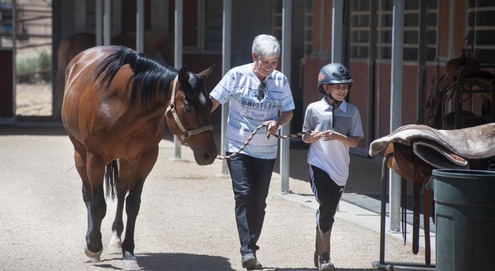A trainer and young client walk alongside a dark brown horse. 