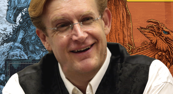 A middle-aged white man in glasses and a black vest poses in front of an illustration of one of his comic book characters