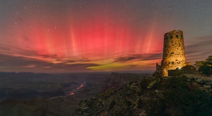 The aurora borealis fills the night sky over the Grand Canyon in a view from Desert View Watchtower, on the East Rim, in October 2024. Far below the rim, the Colorado River mirrors the red hues of the northern lights. | Rich Rudow