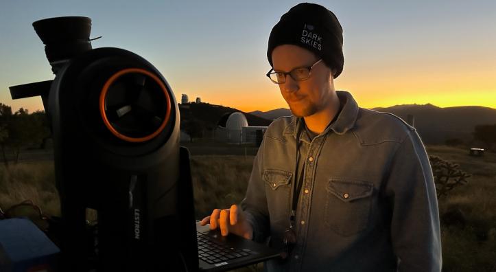 A young man in a black beanie and glasses calibrates a large telescope.