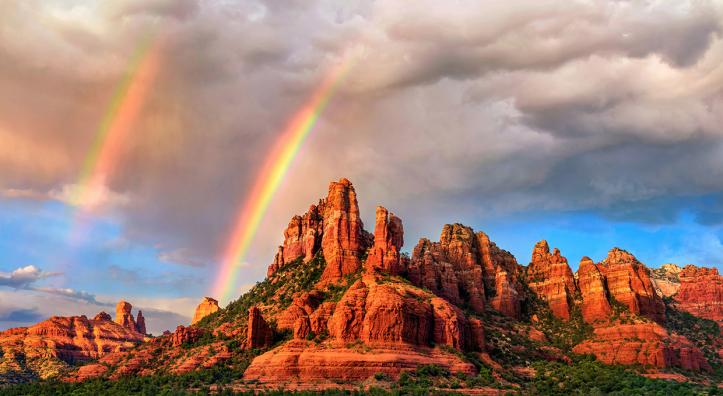 Amid falling rain from an isolated storm cell, a pair of rainbows appear over the sandstone buttes of Red Rock Country at sunset. In theory, all rainbows are double rainbows, but the secondary rainbow is often too faint to be seen. | Theresa Rose Ditson