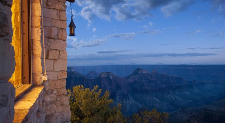 The edge of a building appears in the left of an image that is dominated by the Grand Canyon under an evening sky. 