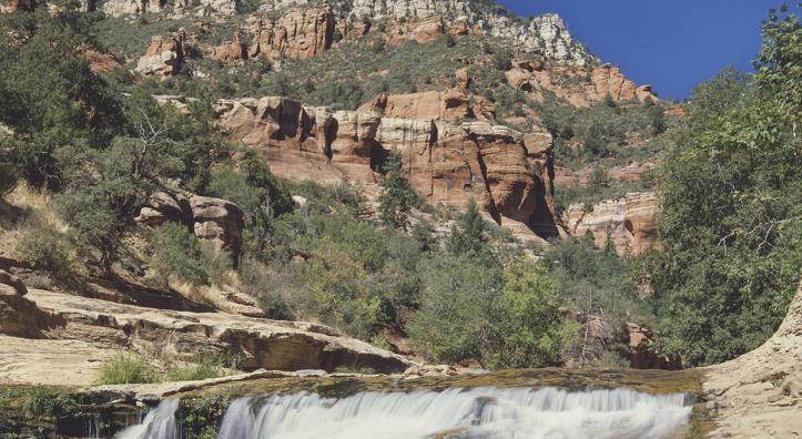 The clear water of Oak Creek tumbles over a small waterfall in the Slide Rock area of Oak Creek Canyon, near Sedona. At the time this photo was made, the Slide Rock area had not yet become an Arizona state park; it received that designation in 1987. By Josef Muench