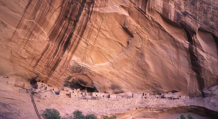 Keet Seel ruins sits perched on a cliff beneath a streak-stained sheer canyon wall. By Laurence Parent