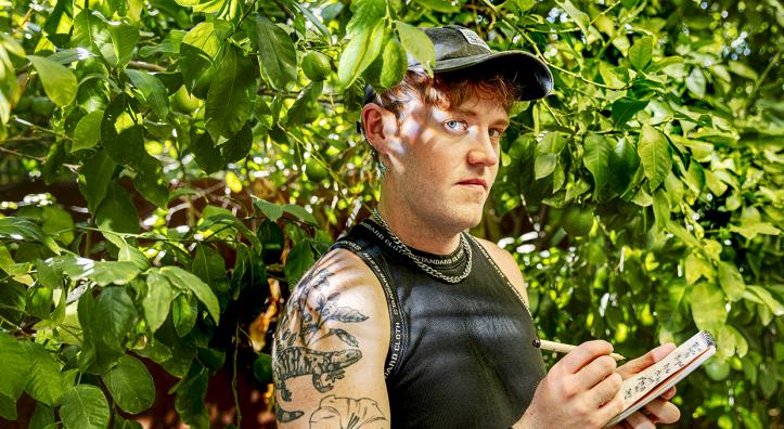 Photograph of Jonathan T. Bailey standing in green foliage while writing in a notepad is by Steven Meckler.