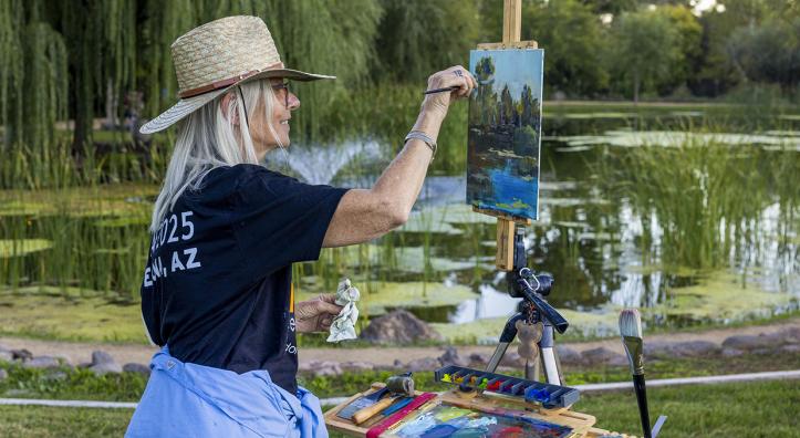 Photograph of a woman painting from an easel outside by a pond is by John Burcham