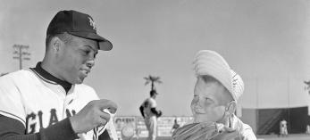 Baseball player wraps a bat as a child looks on.