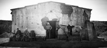 Cowboys stand in front of a ranch building in this black and white photograph