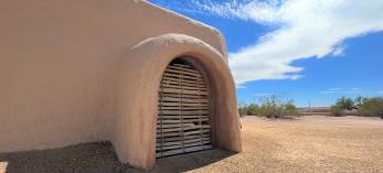The adobe walls of S'edav Va'aki Museum are shown against a bright blue sky with whispy white clouds.