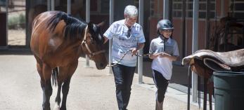 A trainer and young client walk alongside a dark brown horse. 