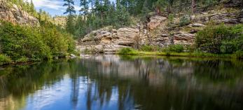 The calm water of East Clear Creek mirrors trees along the Kinder Crossing Trail. By Rebecca Wilks
