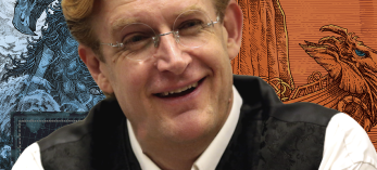 A middle-aged white man in glasses and a black vest poses in front of an illustration of one of his comic book characters