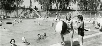 BW photo of two girls with giant beach ball at edge of the pool at Tempe Beach, which is occupied by several other people. Photograph: TEMPE HISTORY MUSEUM