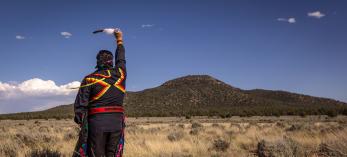 Stuart Chavez, a member of the Havasupai Tribe, raises an eagle feather toward Red Butte, one of the tribe’s sacred sites. By Eirini Pajak