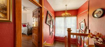 Upstairs hallway, painted red and showing the inside of a guest room and adjacent staircase at the Oliver House. By Steven Meckler