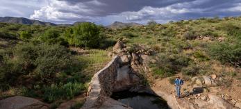 Josiah Austin, owner of the Cienega Ranch in Southeastern Arizona, stands below one of the many check dams he and his employees have constructed on the ranch. In this instance, water retained by the dam has allowed Arizona ash trees and other vegetation to flourish above it.