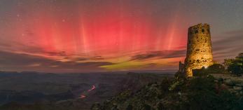 The aurora borealis fills the night sky over the Grand Canyon in a view from Desert View Watchtower, on the East Rim, in October 2024. Far below the rim, the Colorado River mirrors the red hues of the northern lights. | Rich Rudow
