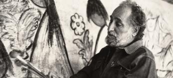 Ted DeGrazia stands with brushes and palette in front of a mural-sized painting. COURTESY OF DeGRAZIA GALLERY IN THE SUN 
