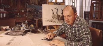 Larry Toschik at his drawing board working on an illustration of water fowl. Portrait of Carlos Elmer with camera. | COURTESY OF THE TOSCHIK FAMILY