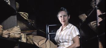 Clara Lee Tanner poses with one of many Native American-made baskets on storage shelves. | HELGA TEIWES/ARIZONA STATE MUSEUM, UNIVERSITY OF ARIZONA