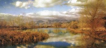 This painterly photograph by Esther Henderson shows autumn foliage and cloudy blue skies reflected in a lake with mountains in the background..