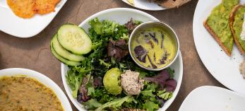 A green salad garnished with cucumbers, guacamole, tuna salad, bread and dressing is the centerpiece of assorted plates that include avocado toast and beans. By Dawn Kish
