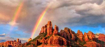 Amid falling rain from an isolated storm cell, a pair of rainbows appear over the sandstone buttes of Red Rock Country at sunset. In theory, all rainbows are double rainbows, but the secondary rainbow is often too faint to be seen. | Theresa Rose Ditson