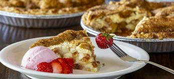 A slice of pie with strawberry slices and ice cream is plated along side severa whole pies. By Steven Meckler