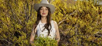 Stina Swesey poses in a desert setting holding a bunch of creosote flowers. By Steven Meckler