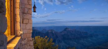 The edge of a building appears in the left of an image that is dominated by the Grand Canyon under an evening sky. 