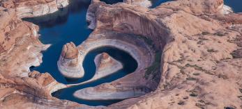 An aerial photo of Lake Powell’s Reflection Canyon displays the reservoir’s current and former water levels, along with the canyon’s looping course. By Gary Ladd