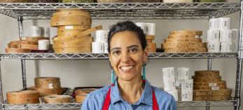 Amy Valdés Schwemm spoons mole powder into dozens of tins in front of ingredient racks. By Steven Meckler