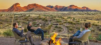 Photograph of four people sitting around a fire at dusk with a view of the nearby Santa Rita Mountains is by Steven Meckler.