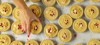 Photograph of a hand reaching for a small, decorative pie among dozens is by Steven Meckler