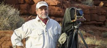 Portrait of Gary Ladd with 4x5 camera against a backdrop of red rocks is by Renee Roundtree.