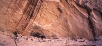 Keet Seel ruins sits perched on a cliff beneath a streak-stained sheer canyon wall. By Laurence Parent