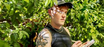 Photograph of Jonathan T. Bailey standing in green foliage while writing in a notepad is by Steven Meckler.